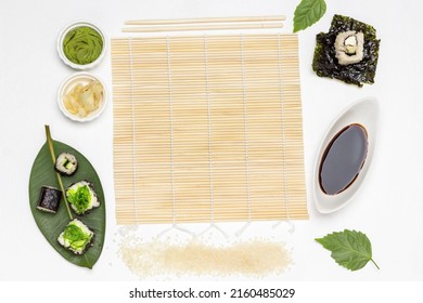 Flat Lay Sushi Making Process. Bamboo Mat, Rice, Soy Sauce And Nori Leaves. White Background