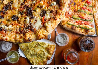 flat lay of a table, two different leves of pizza, 3 kinds of pizza. wood table with sodas an d salt and pepper