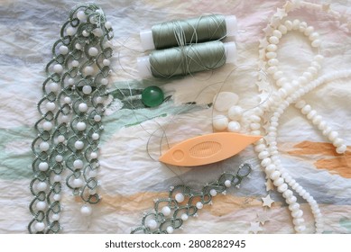 Flat lay of tatting lace in progress with shuttle, thread spools, beads and gemstones on soft fabric. Handmade lace making supplies in natural light.