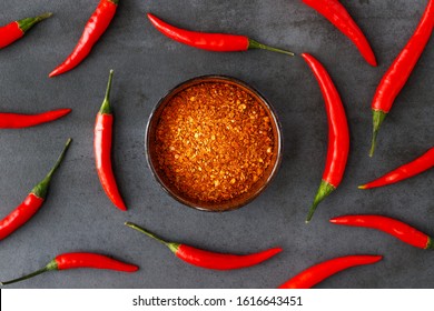 Flat lay of Thai red fresh hot chilli peppers with green tails and dried red chilli flakes in bowl on black stone background. Food pattern. Popular spices. 
