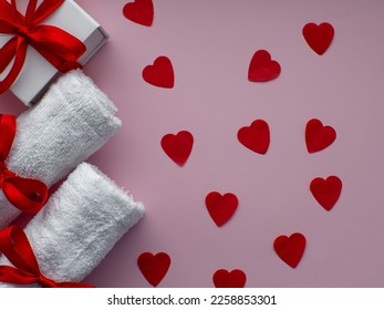 Flat lay with a lot of tiny heart-shaped papers, two towels and gift box. Red heart paper background with towels tied with a red bows. Valentines day spa, bath, self care and body care concept.