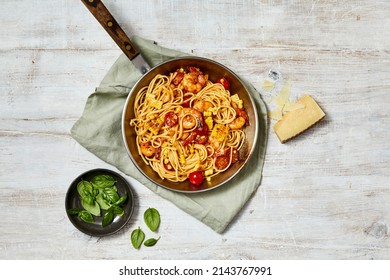 Flat Lay Top Down Food Photography Of A Prawn And Cherry Tomato Fettucine Pasta Dish In A Pan With Ingredients Of Basil And Parmesan Cheese On A White Wash Timber Background.