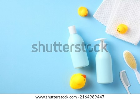 Flat lay, top view baby shampoo bottle, body wash gel, towel, hair comb, brush, yellow rubber ducks on blue background. Baby bathing concept.