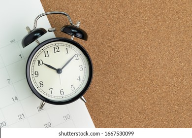 Flat lay or top view  of black alarm clock with white calendar on wooden pin board with copy space, schedule for vacation, reminder for business appointment or deadline for business project.
