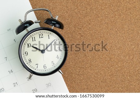 Flat lay or top view  of black alarm clock with white calendar on wooden pin board with copy space, schedule for vacation, reminder for business appointment or deadline for business project.
