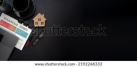 Flat lay of top view black desk work table with house model computer laptop and financial newspapaer in Real estate market concept includes copyspace for add text or graphic