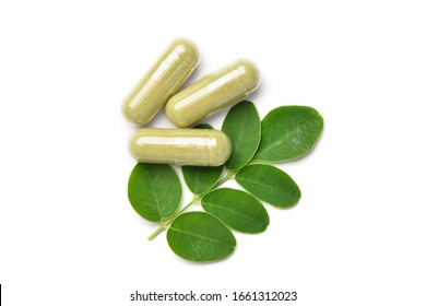 Flat lay (top view) of Dried Moringa leaves powder capsules with fresh green leaves  isolated on white background.