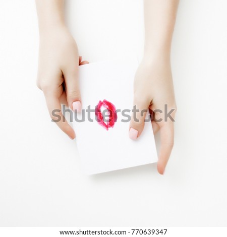 Flat lay. Top view. Hand of girl writing love letter on Saint Valentines Day. Handmade postcard with red lips shaped figure. Woman draw kiss on postcard for 14 February holiday celebration