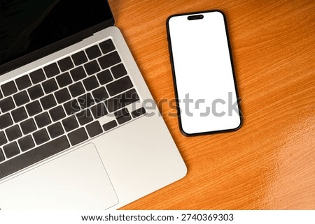 Flat lay top view of modern workspace featuring a silver laptop, blank screen tablet for mockup, and wireless earbuds on a brown wooden desk. Concept for remote work, online learning, and digital noma