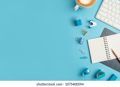 Flat Lay, Top View Office Table Desk. Workspace With Blank Note Book, Keyboard, Blue Office Supplies And Coffee Cup On White Background.