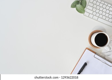 Flat lay top view office desk. Workspace with blank clip board, computer keyboard, office supplies, pen, green leaf, and coffee cup on white background.