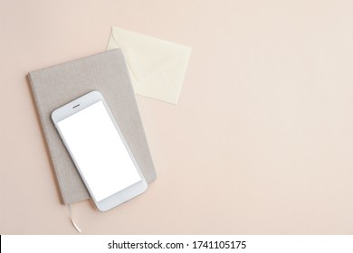 Flat Lay, Top View Office Desk Table With Mobile Phone Mockup With Blank White Screen, Paper Notebook And Envelope On Beige Background. Business And Technology Concept.