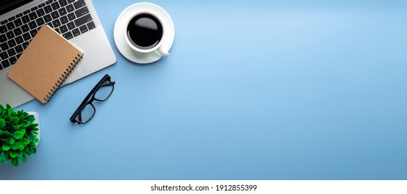 Flat lay, top view office table desk. Workspace with, laptop,office supplies, pencil, green leaf, and coffee cup on blue background.
