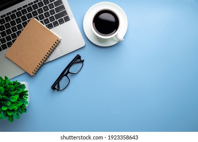 Flat lay, top view office table desk. Workspace with, laptop,office supplies, pencil, green leaf, and coffee cup on blue background.
