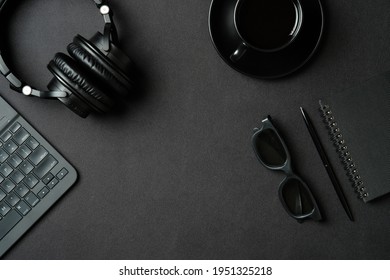 Flat lay top view office desk. Workspace with laptop computer, headphones, coffee cup, paper notebook, pen, glasses on black table. - Shutterstock ID 1951325218