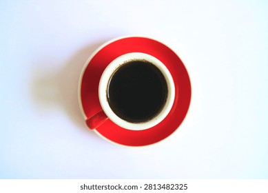 Flat lay top view of a red ceramic espresso cup filled with dark black coffee on a saucer, minimalist studio shot isolated on clean white background