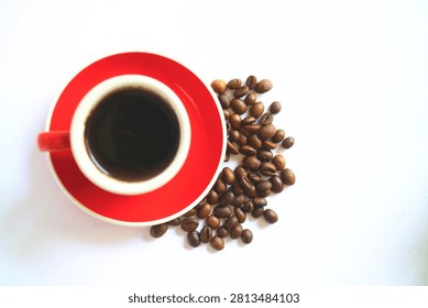 Flat lay top view of a red ceramic espresso cup filled with black coffee placed next to a pile of roasted coffee beans, isolated on a white background