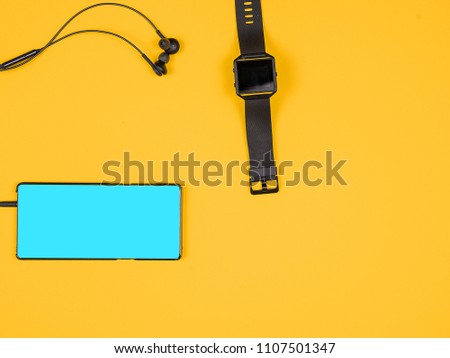 Flat lay top view of smartphone with headphones in it and smartwatch. Design and concept. Orange background