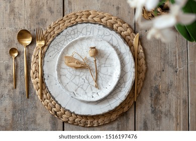 Flat lay and top view of table setting on wooden background. White plates, tableware, cutlery spoon with fork, knife lying on woven rug with decorative elements and fresh orchid flower