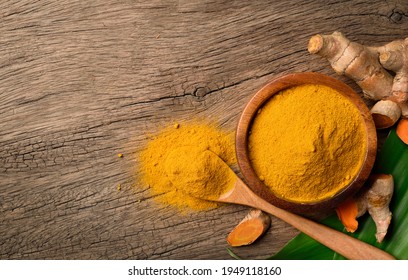 Flat Lay (top View) Of Turmeric (curcumin) Powder In Wooden Bowl And Spoon With Fresh Rhizome On Wood Background.