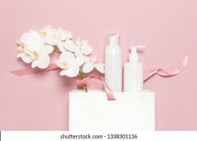 Flat lay top view White cosmetic bottle containers gift bag White Phalaenopsis orchid flowers on pink background. Cosmetics SPA branding mock-up Natural organic beauty product concept Minimalism style