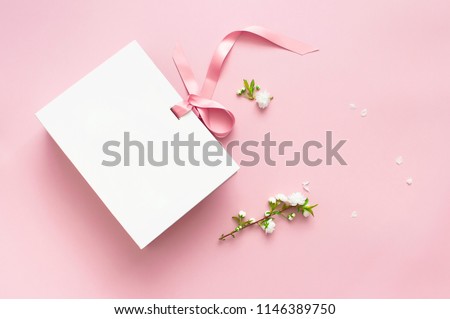 Flat lay top view White gift bag and spring flowers on a pink background. Greeting card with delicate flowers Pink floral background with copy space