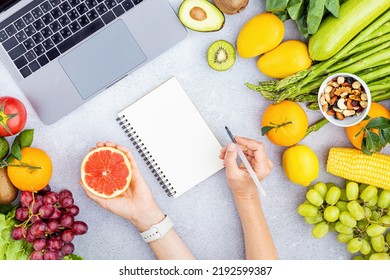 Flat Lay Top View Of Woman Holding Hand Sliced Grapefruit And Filling Weekly Meal Plan On Gray Background With Laptop, Fresh Fruits And Vegetables. Calories Control, Meal Plan, Food Diet And Weight