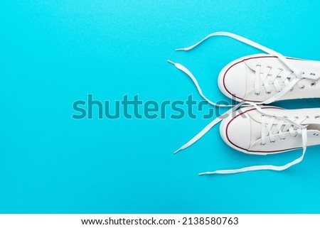 Flat lay top-down composition of pair of white untied sneakers. Minimalist flat lay image of white gumshoes over turquoise blue background with copy space. 商業照片 © 
