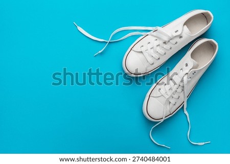 Flat lay top-down composition of pair of white untied sneakers. Minimalist flat lay image of white gumshoes over turquoise blue background with copy space.