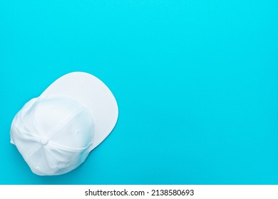Flat lay top-down composition of white snapback cap. Minimalist flat lay photo of white cap with copy space. Top view of baseball cap over torquoise blue background.