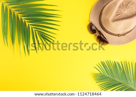 Flat lay Travel  acessories with tropical palm leaves,glasses,straw hat on yellow background.