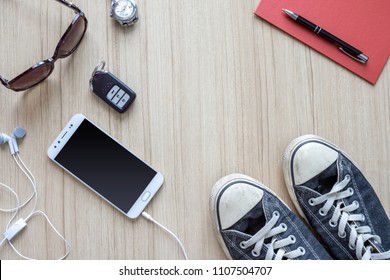 Flat lay traveler accessories on wooden floor background with remote car, smartphone, earphones , pen, paper note , shoes and sunglasses. Top view travel or vacation concept. 