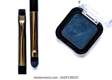 Flat lay of two parallel eyeshadow brushes and a gray-blue eyeshadow palette on white background. Minimalist beauty and makeup concept with soft focus and artistic balance.
