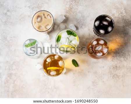 Flat lay of various refreshing drinks in glasses with ice. Apple juice, homemade lemonade, iced coffee, iced tea and sparkling water on beige background. Top view
