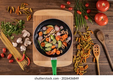 Flat lay of vegetables and food and a frying pan with food over a wooden table