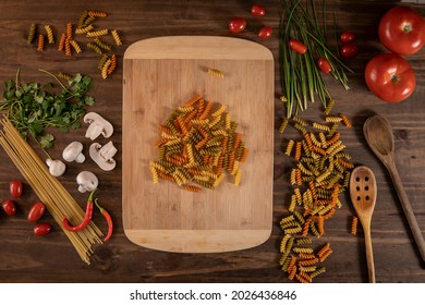 Flat lay of vegetables and pasta and a chopping table over a wooden table