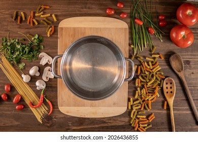 Flat lay of vegetables and pasta and a chopping board with a cacerola over a wooden table
