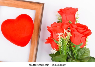 Flat lay view of artificial red roses with heart shape and wooden frame on white background. Love and Valentine's Day concept. Selective focus.