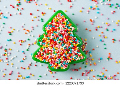 Flat Lay View Of Christmas Tree Shaped Cookie Cutter Filled With Rainbow Sugar Sprinkles With Copy Space.