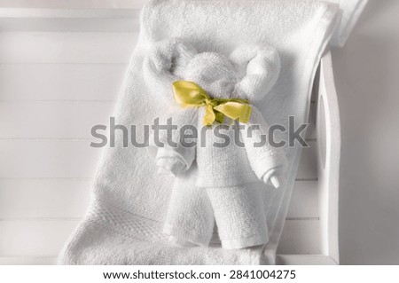 Flat lay view of a cute bear shaped animal folded from a white hand towel, placed on a white tray in a bathroom. Known as towel origami towel animal.