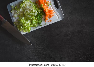 Flat lay view of a knife leaning against a plastic cutting board with finely chopped vegetables (carrots, spring onions and lettuce) on it.