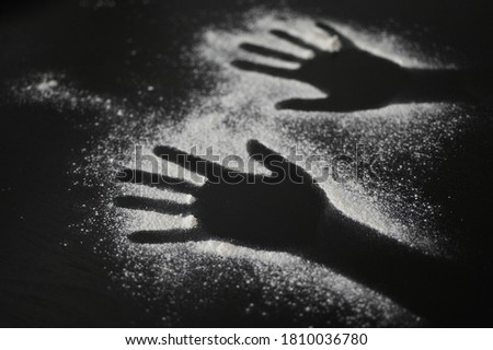 Flat lay view of plain flour in a shape of human hands on black wooden table.