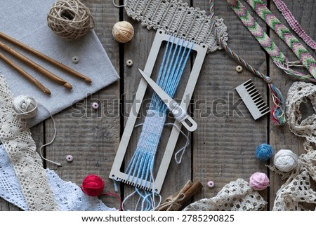 Flat lay weaving and macrame workspace with loom shuttle threads crochet hooks comb lace and craft accessories on rustic wooden table background