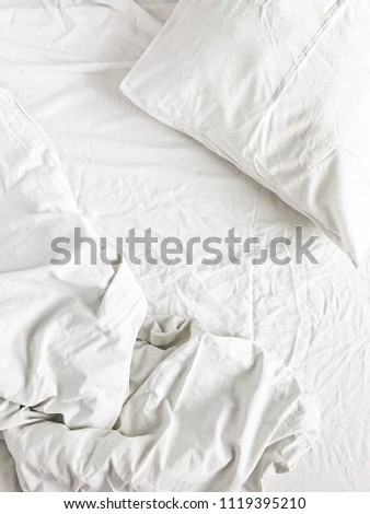 Flat lay of white bed with pillows, blanket and sheet. Top view minimal linen concept.