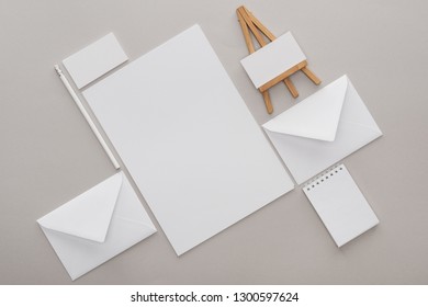 flat lay with white empty papers and letters with toy easel at workplace on grey background