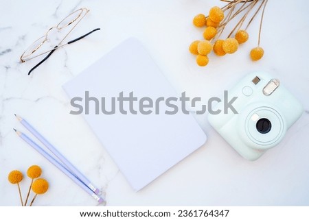 Flat lay of white marble table with stationery, glasses, yellow flowers and photo camera. Top view with copy space. Modern female work place concept