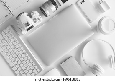 Flat lay of white office desk table with many white gadgets laptop computer, digital camera, headphone, smartphone, external harddrive etc.
