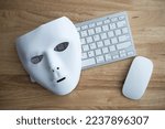 Flat lay white scary half face mask, keyboard and mouse on wooden table background in dark tone. Hacker, cybercrime, romance scam and online security concept.