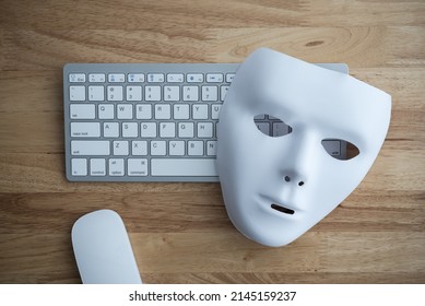 Flat lay white scary half face mask, keyboard and mouse on wooden table background in dark tone. Hacker, cybercrime, romance scam and online security concept.