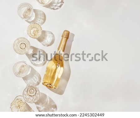 Flat lay with white sparkling wine bottle, set glasses wine with sunshine shadow and flare on light beige background. White wine aesthetic photo, copyspace. Summer holiday monochrome color still life
